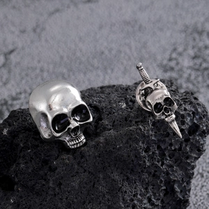 Macro view of gothic skull and dagger asymmetric earring set on volcanic stone