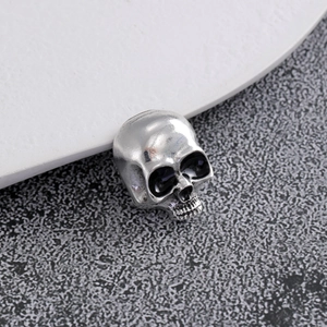 Macro shot of silver skull charm with black enamel eyes on a grey textured background