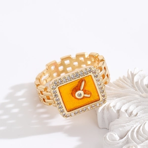Dettaglio dell'anello dorato ispirato all'orologio con quadrante arancione e strass