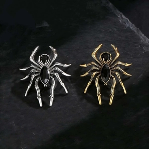 Close-up of gold and silver spider brooches with black marquise stones on rock