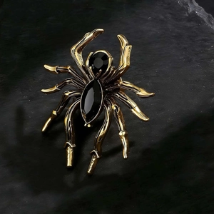 Detailed view of a gold-plated spider brooch with black gemstones on a stone surface