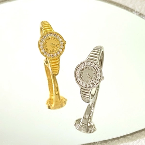 Dettaglio di due anelli a forma di orologio in oro e argento con pavé di piccoli cristalli