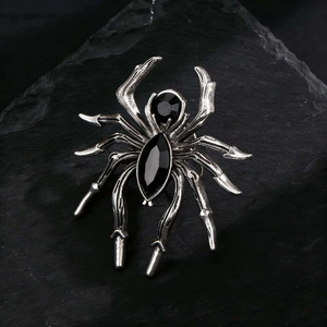Macro shot of silver spider brooch featuring black faceted gemstones on textured rock