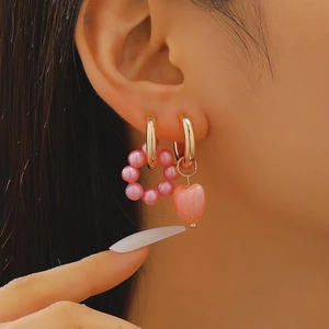 Close-up of pink heart pearl earrings with long asymmetric charms on a model