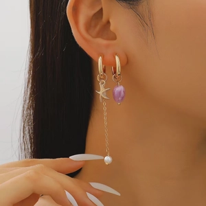 Close-up of asymmetrical gold earrings featuring starfish charms, purple gems and pearls