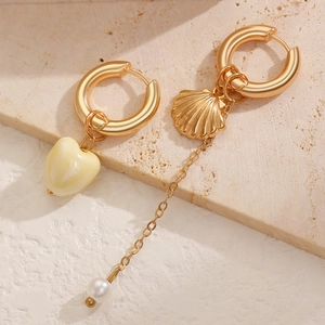 Detail of asymmetrical gold hoop earrings with heart, shell charms and white pearl drop