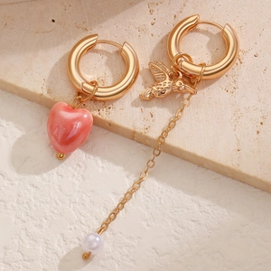 Detail of asymmetric gold earrings with pink heart and bird pearl drop pendants