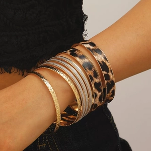 Detailopname van meerlagige armbandenset met luipaardprint leer en gouden legering om de pols