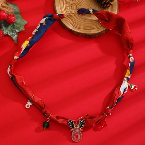 Détail du collier de Noël en soie avec breloques renne et sapin sur fond rouge festif