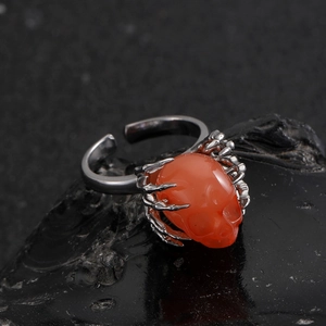 Gothische schedelring met oranjerode steen en zilveren klauwen op donkere minerale steen