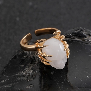 Detailopname van een gouden gotische ring met een witte schedelsteen en skeletachtige klauwen