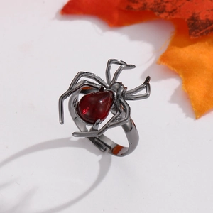 Close-up of gothic spider ring with deep red gemstone on metal leaf background