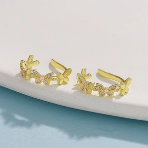 Macro detail of gold butterfly ear clips with pink zircons on a white stone display