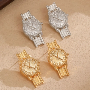 Detail of unique watch-shaped metal earrings in gold and silver finishes on beige stone
