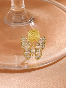 Macro shot of gold butterfly ear clip with zircons on elegant champagne silk fabric