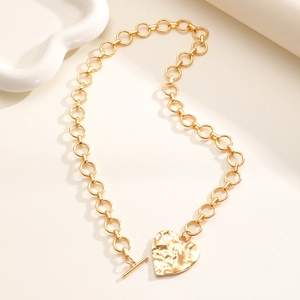Dettaglio del ciondolo a cuore dorato con texture martellata e collana con chiusura a T