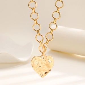 Dettaglio del ciondolo a cuore in oro martellato con chiusura a T dal design moderno