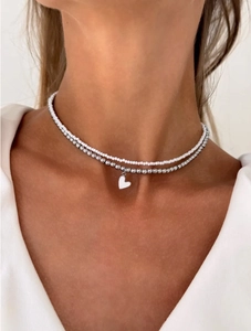 Close-up of double-layered beaded necklace with white heart pendant on model's neck