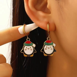 Primo piano di un modello che indossa orecchini a pinguino di Natale in smalto dorato