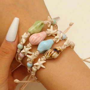 Detailed view of four handmade ocean-themed bracelets with ceramic shells on a wrist