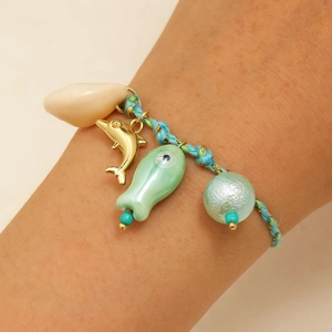 Detail of hand-woven bracelet with ceramic fish and gold dolphin charms on wrist
