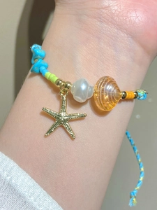 Macro shot of hand-painted ceramic starfish charm and shell beads on a blue woven bracelet