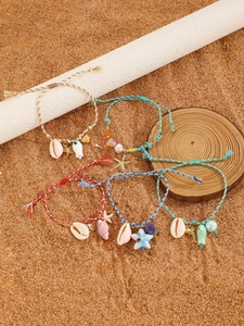 Detail of five handmade woven starfish bracelets with shell charms on a sandy beach