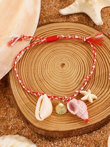 Detail of hand-woven ocean charm bracelet with ceramic starfish and shell on sand