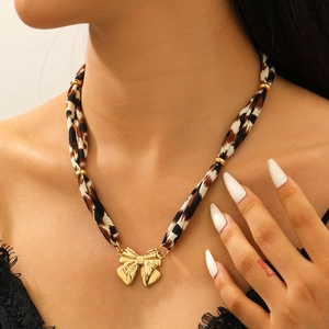 Gros plan du collier en tissu léopard avec pendentif nœud doré et perles métalliques
