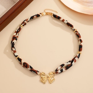 Détail d'un ras-de-cou léopard avec pendentif nœud doré et perles sur un fond beige doux
