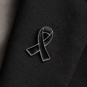 Black awareness ribbon lapel pin with silver trim on a dark suit fabric background