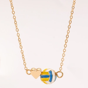 Detailansicht des goldenen Herzanhängers und des blau-gelben Emaille-Volleyballs