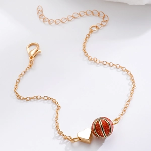 Detailansicht von Herzanhänger und rotem Glitzerball an einer feinen goldenen Kette