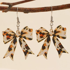Creative leopard print bow earrings made of acrylic hanging on a rustic dry branch