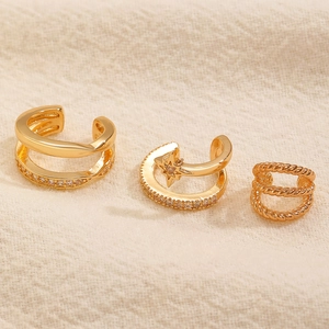 Set di tre ear cuff dorati con motivi a stella e zirconi su tessuto beige