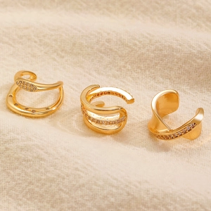 Set di tre ear cuff placcati oro con strass su sfondo di tessuto a trama strutturata