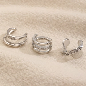 Dettaglio macro di tre ear cuff in argento con disegni geometrici scintillanti con diamanti