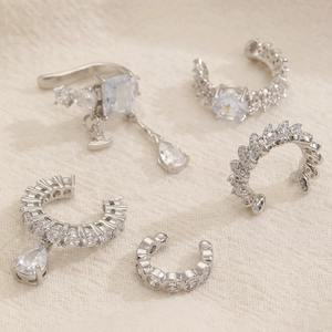 Dettaglio di cinque earcuff in argento con zirconi scintillanti su sfondo in tessuto beige