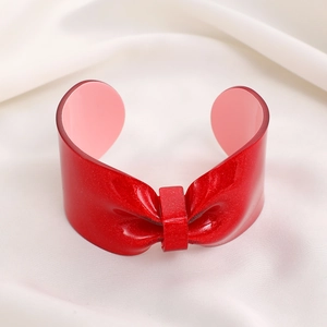 Detailed view of bold red glitter bow cuff bracelet on white silk fabric background