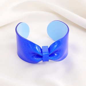 Detail shot of blue glitter resin bow cuff bracelet on white silk satin background