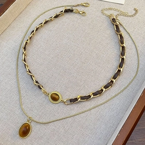 Details der goldenen Schlangenkette und des braunen Leder-Halsbands mit Tigerauge