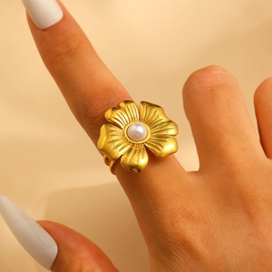Detailed view of an 18k gold floral ring with a central pearl on a model's hand