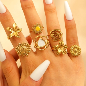 Detail of seven gold-colored floral rings with enamel accents on a model's hand