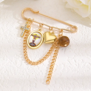 Détail d'une broche dorée avec pendentif croix, breloque coeur et médaille religieuse