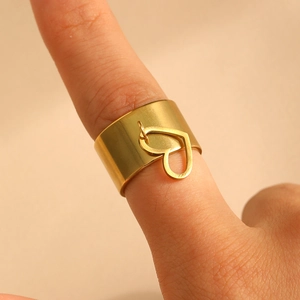 Dettaglio macro di anello largo dorato in acciaio con piccolo ciondolo a cuore decorativo