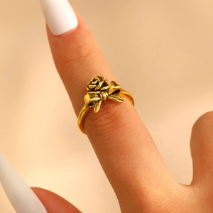 Close-up of golden rose and bowknot ring design on finger with a minimalist background