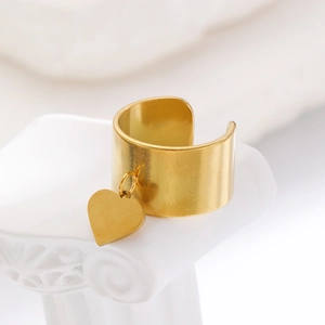 Primo piano di un ampio anello in acciaio dorato con dettaglio di pendente a cuore