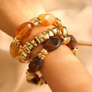 Detail of stacked vintage resin and gold chain bracelets on a model's wrist