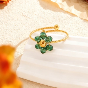 Detailansicht eines goldfarbenen Rings mit strukturierter Oberfläche und grüner Kristallblume