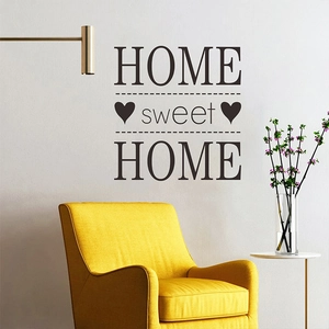 Détail du sticker mural SWEET HOME marron foncé sur mur blanc au-dessus d'un fauteuil